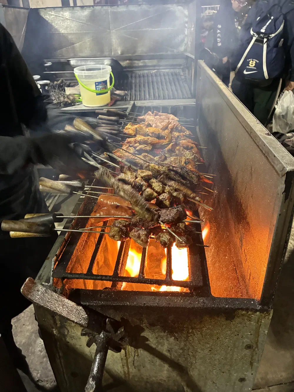 Rows of beef and chicken kebabs cooking over an open coal grill
