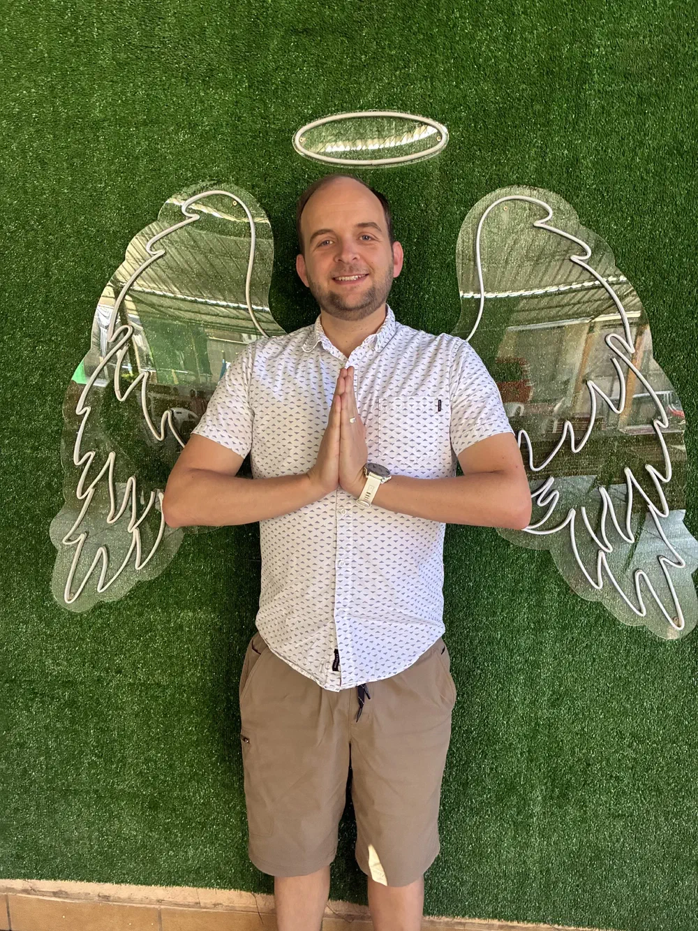 A man standing in front of a neon angel-wings mural on an artificial grass wall