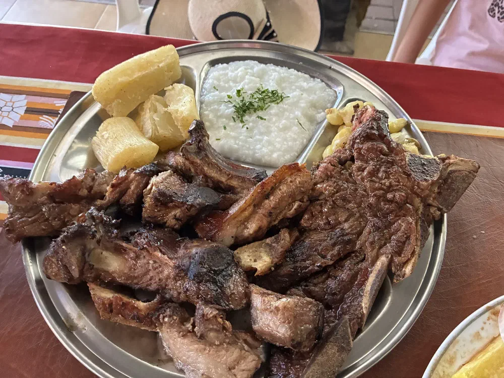 A steel platter of grilled ribs and steak with boiled yuca and cheesy rice