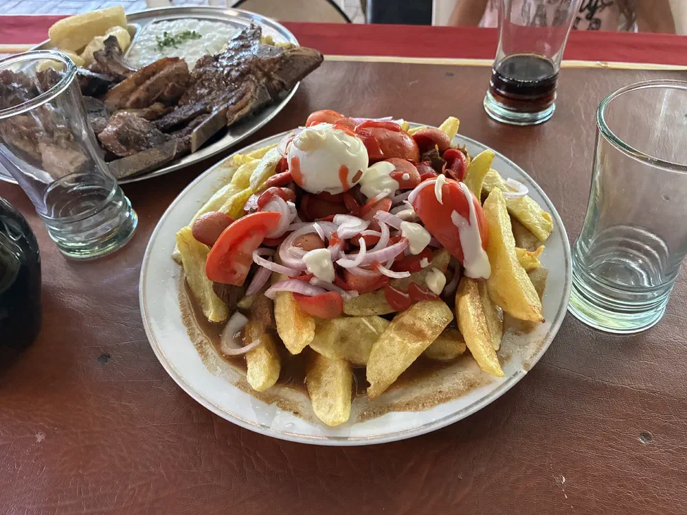 A plate of thick-cut fries topped with tomato, sliced onion and mayonnaise