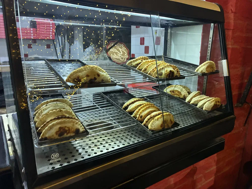 A lit glass warming case holding rows of baked empanadas on steel racks