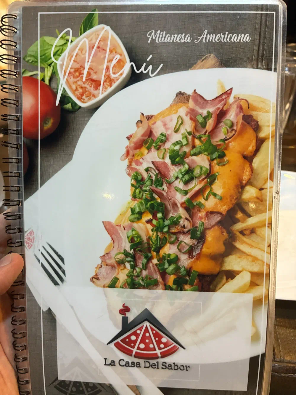 The spiral-bound menu cover, showing a milanesa americana topped with bacon, cheese sauce and spring onion