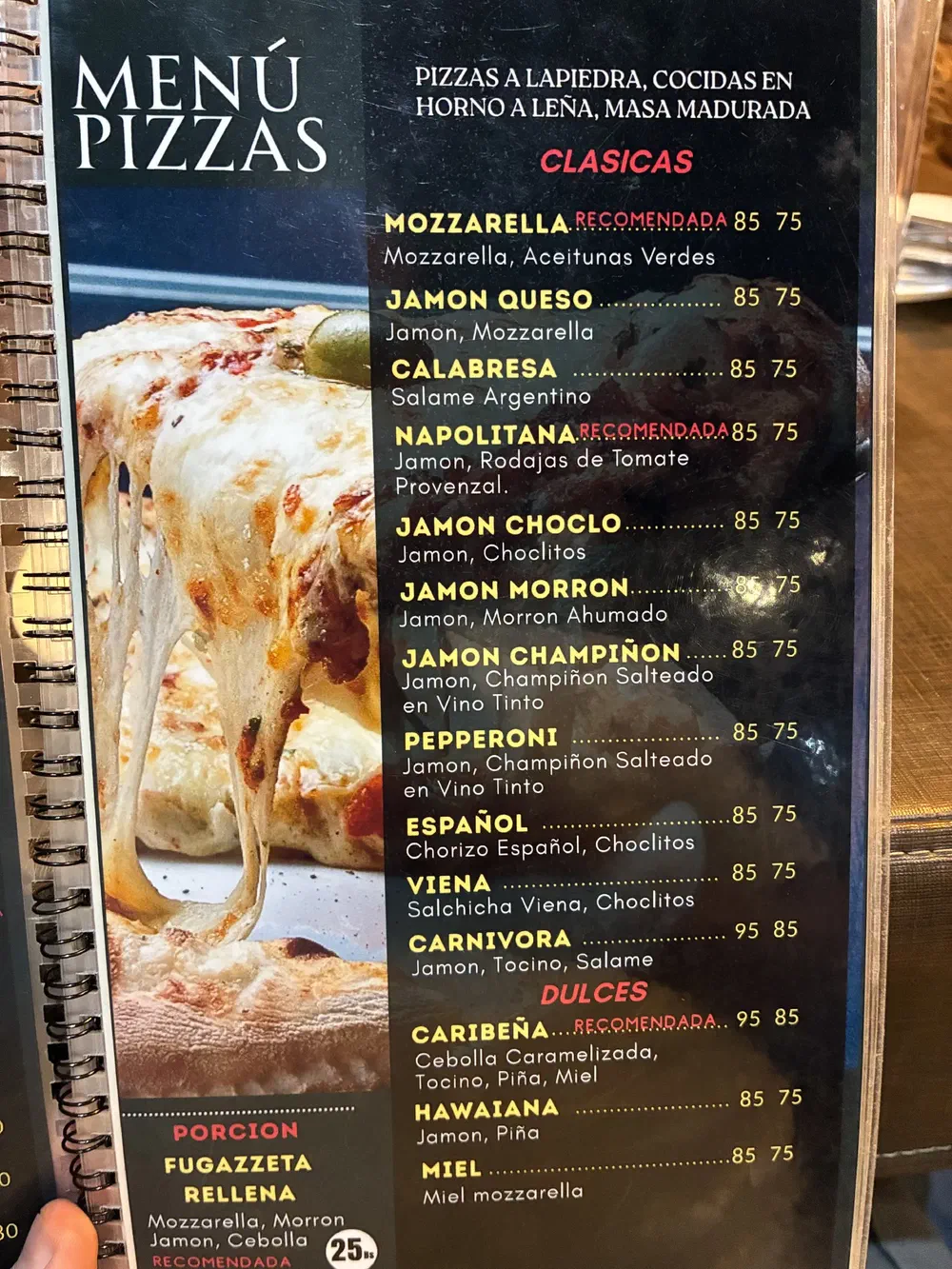 Pizza menu page listing the Clasicas and the sweet Dulces, beside a photo of a cheese pizza slice being lifted